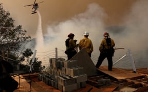 A firefighting helicopter drops water on the Palisades Fire on January 11, 2025 in Los Angeles, California. The Palisades fire had grown to over 22,000 acres and has destroyed thousands of homes. The fire is currently 11 percent contained