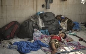 A child sleeps along the roadside where thousands are living with out shelter and exposed to the elements following the burning down of their camp.