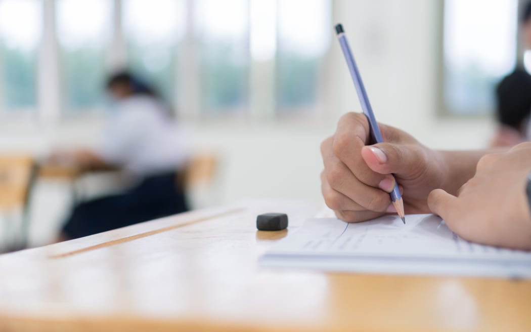 Side view of high school or university student writing on a paper in a classroom.