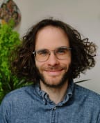 Mid-shot of NPR Podcast host Darian Woods who has long curly hair and wears glasses