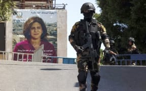 Palestinian security officers stand guard across from a banner depicting slain Palestinian-American journalist Shireen Abu Akleh near the Church of the Nativity in Bethlehem in the occupied West Bank, on July 15, 2022, ahead of the arrival of the US President for an official visit. (Photo by ABBAS MOMANI / AFP)