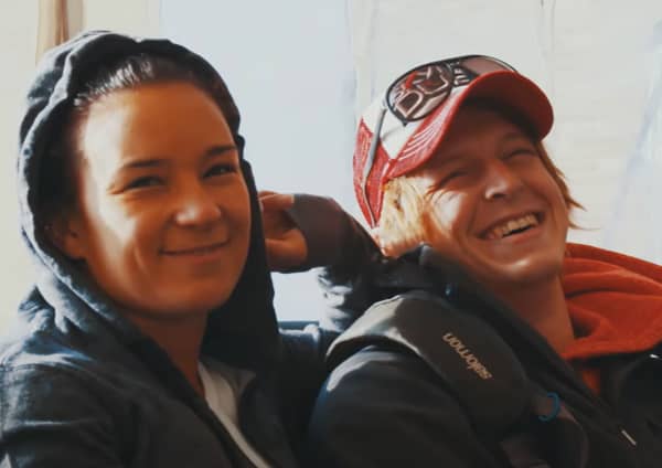 Two smiling young people - a woman wears a hoodie and man wears a trucker cap.