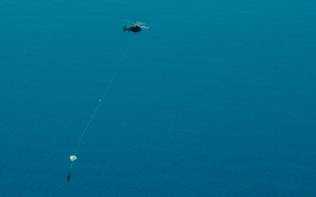 A helicopter carrying a big cylinder on a line.