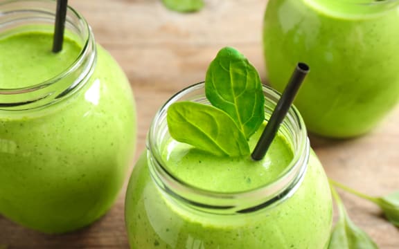 Jars of healthy green smoothie with fresh spinach on wooden table, closeup view