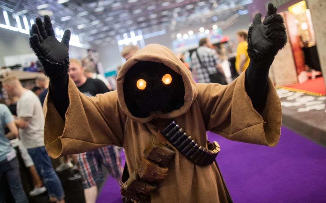 A cosplayer dressed as a Star Wars Jawa character walks over the grounds of the "Comic Con Experience" (CCXP) fair on the world of comics and movies on June 27, 2109 in Cologne, western Germany. According to organisers, "setups from studios, publishing houses, companies fan groups and cosplayers will carry off visitors into universes familiar from film, series, comics and books" during the fair running from June 27 to 30, 2019. (Photo by Rolf Vennenbernd / dpa / AFP) / Germany OUT