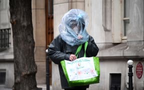 As anxiety increases, a man protects his face with a plastic bag as he walks in the street in Paris.