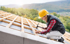 Female worker on the building site. Young woman working as a roofer. House construction.