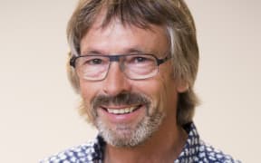 A headshot of a smiling man with sandy brown hair, facial hair and glasses.