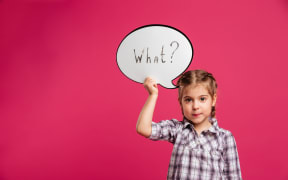 Image of pretty little girl child standing isolated over pink background. Looking camera holding speech bubble.