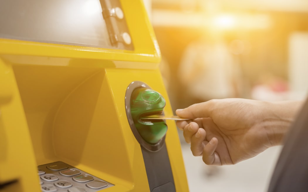 Person inserting bank card into ATM machine to withdraw money.