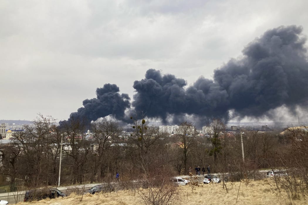 A picture taken on March 26, 2022 shows a religious statue as dark smoke rises from a fire following an air strike in the western Ukrainian city of Lviv.