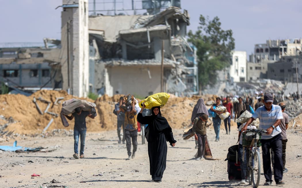 People walk along a heavily-damaged road past destroyed buildings in the centre of Khan Yunis in the southern Gaza Strip on October 10, 2025, as the displaced return to their homes after Israeli forces' withdrawal. Gaza's civil defence agency said on October 10 that Israeli forces have begun pulling back from parts of the territory, particularly in Gaza City and Khan Yunis. Israeli forces declared a ceasefire and withdrew from some positions as thousands of displaced Palestinians began to trek home and the families of October 7 hostages awaited news. (Photo by Omar AL-QATTAA / AFP)