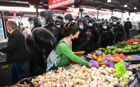 A woman continues to shop for vegetables as riot police clear Melbourne's Queen Victoria Market of anti-lockdown protesters during a rally on September 13, 2020, amid the ongoing COVID-19 coronavirus pandemic.