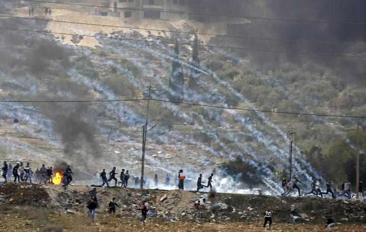 Palestinian protesters run for cover amidst smoke during clashes with Israeli security forces, as protests continue in the region over US President Donald Trump's recognition of Jerusalem as its capital.