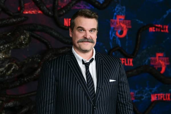 David Harbour, with a moustache and pinstripe suit, smirks for photographers.