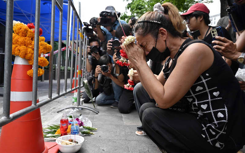 A woman, identified as Nid, prays for her deceased daughter Namtip Tubsook and her son-in-law Suwitcha Sirililung in front of the Rong Beer Na Lat Phrao bar in Bangkok on July 14, 2026. Investigators combed on July 13 through the wreckage of a huge fire at a Bangkok bar that killed at least 28 people, as relatives began the grim task of identifying the dead. (Photo by Lillian SUWANRUMPHA / AFP)