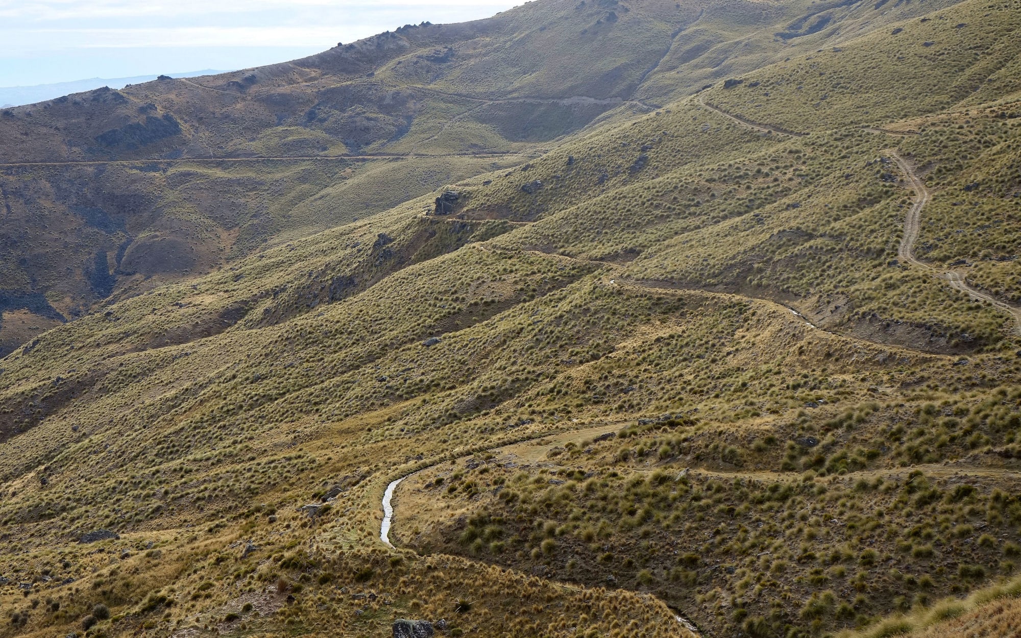 Small hand dug water channel winds down dry brown hillside