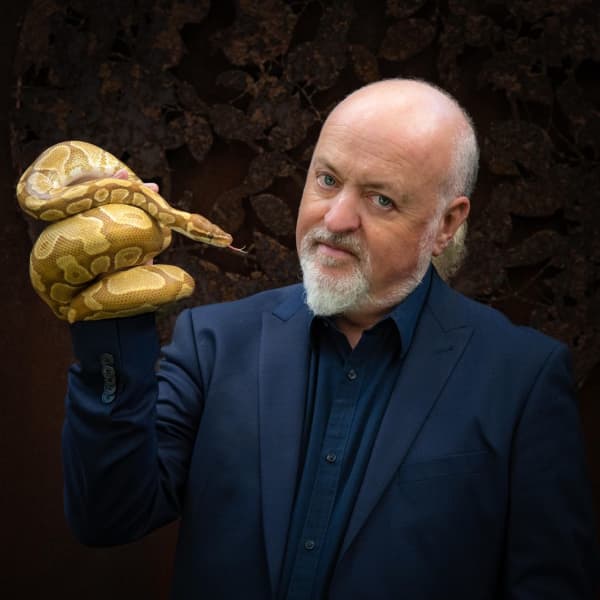 Bill Bailey holds a yellow snake.