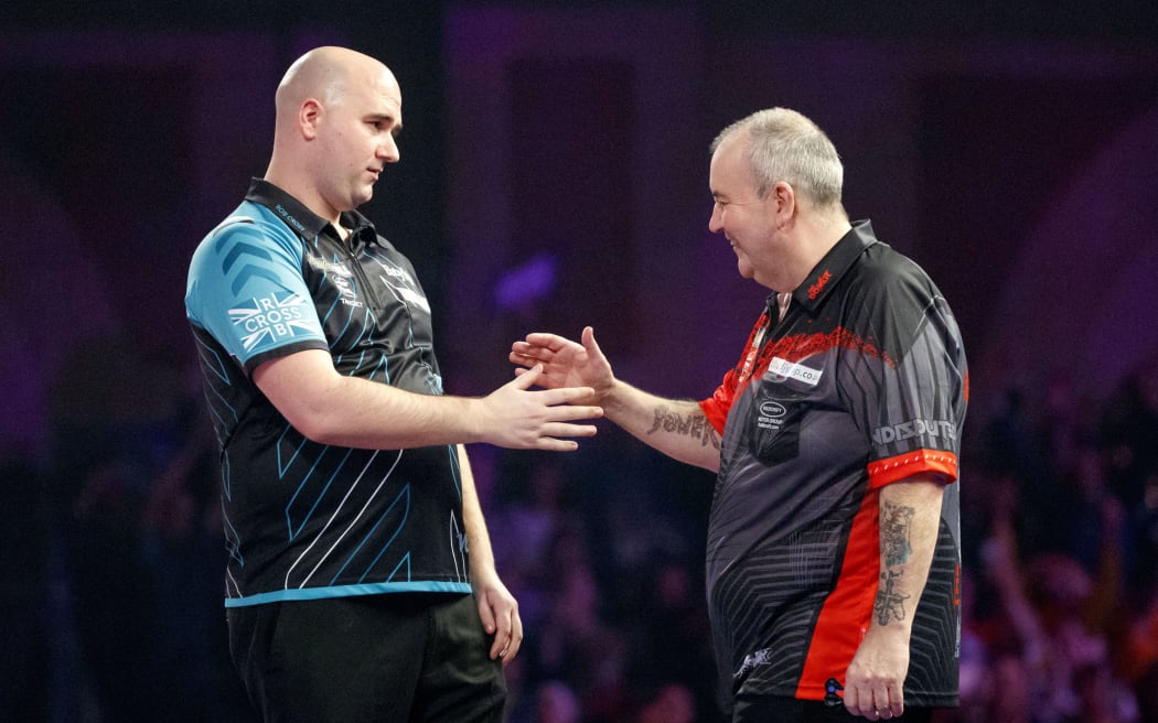 English professional darts player, Rob Cross (L) reacts after beating English professional darts player, Phil Taylor (R) at the PDC World Darts Championship 2018 final game in London on January 1, 2018.