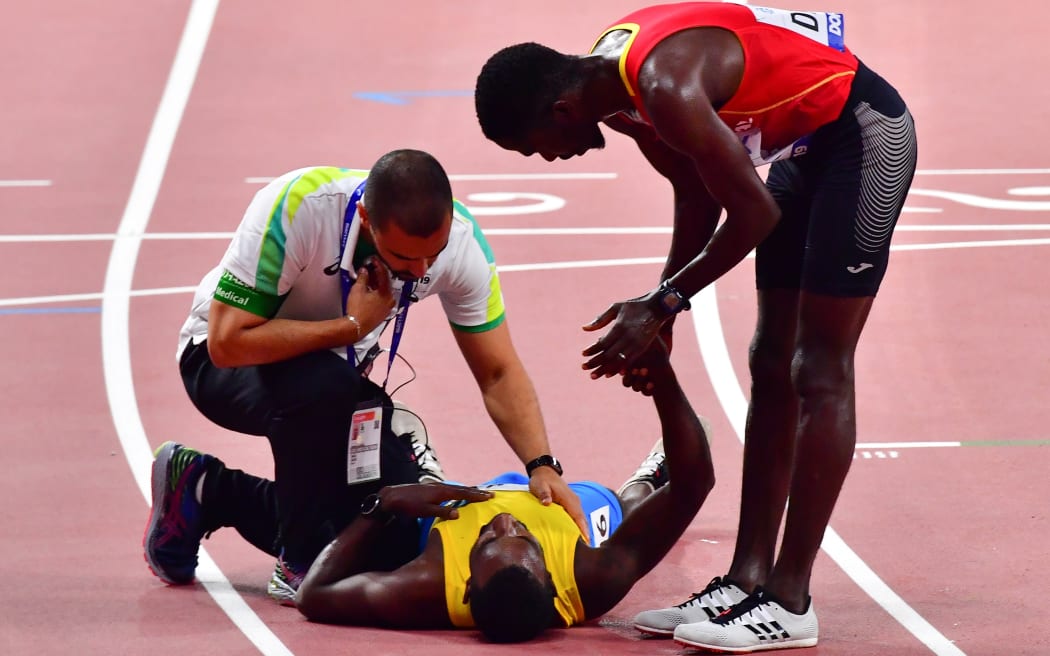 Aruba's Jonathan Busby (L) collapses after crossing the finish line in the hands of Guinea-Bissau's Braima Suncar Dabo during the Men's 5000m heats at the 2019 IAAF World Athletics Championships at the Khalifa International stadium in Doha on September 27, 2019. (Photo by Giuseppe CACACE / AFP)