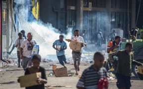 People run with merchandise as crowds leave shops with looted goods amid a state of unrest in Port Moresby on January 10, 2024. A festering pay dispute involving Papua New Guinea's security forces on January 10 sparked angry protests in the capital, where a crowd torched a police car outside the prime minister's office. By Wednesday afternoon pockets of unrest had spread through the capital Port Moresby, with video clips on social media showing crowds looting shops and stretched police scrambling to restore order. (Photo by Andrew KUTAN / AFP)