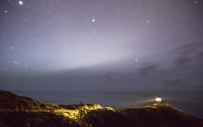 A serene night sky filled with stars above a lighthouse illuminating the coastline, Cape Reinga, New Zealand (Photo by Peter Evans / Connect Images via AFP)