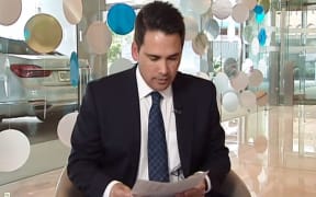 Simon Bridges looks at Newshub;s leaked list of his travel expenses during Monday's exclusive report  - with his crown car in the background.