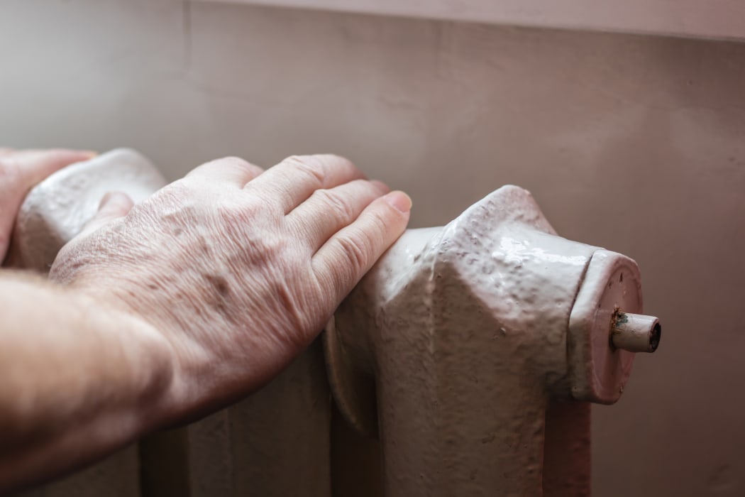An elderly man warms his hands on the Central heating battery.