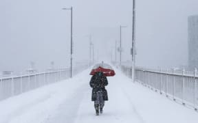 A person crosses the Brooklyn Bridge during a winter storm in New York City on February 23, 2026. New York ordered drivers off the road and shut down schools on Monday, while residents hunkered down for a massive snowstorm hitting the United States northeast. The National Weather Service (NWS) said in a post on X that "heavy snow is still falling" at 5:28 am local time (1028 GMT) on Monday adding that a the total snowfall stands at 14.9 inches. (Photo by ANGELA WEISS / AFP)