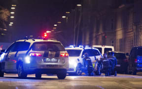 Police officers take cover behind their patrol cars after one person was shot in the head and two policemen were shot in the arm and leg in Krystalgade.