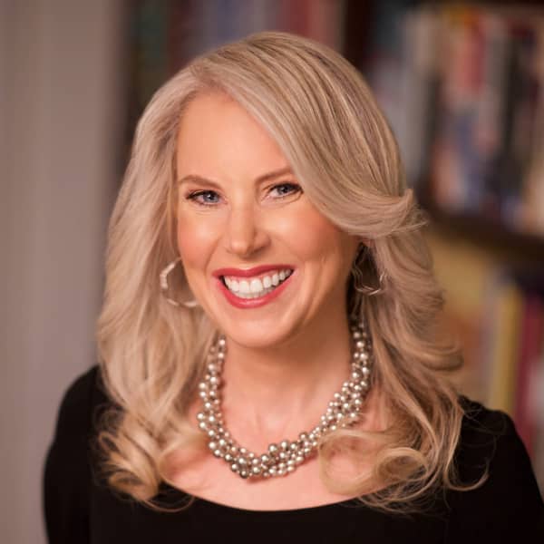 Jocelyn Elise Crowley  is a smiling woman with a pearl necklace and blonde wavy hair.