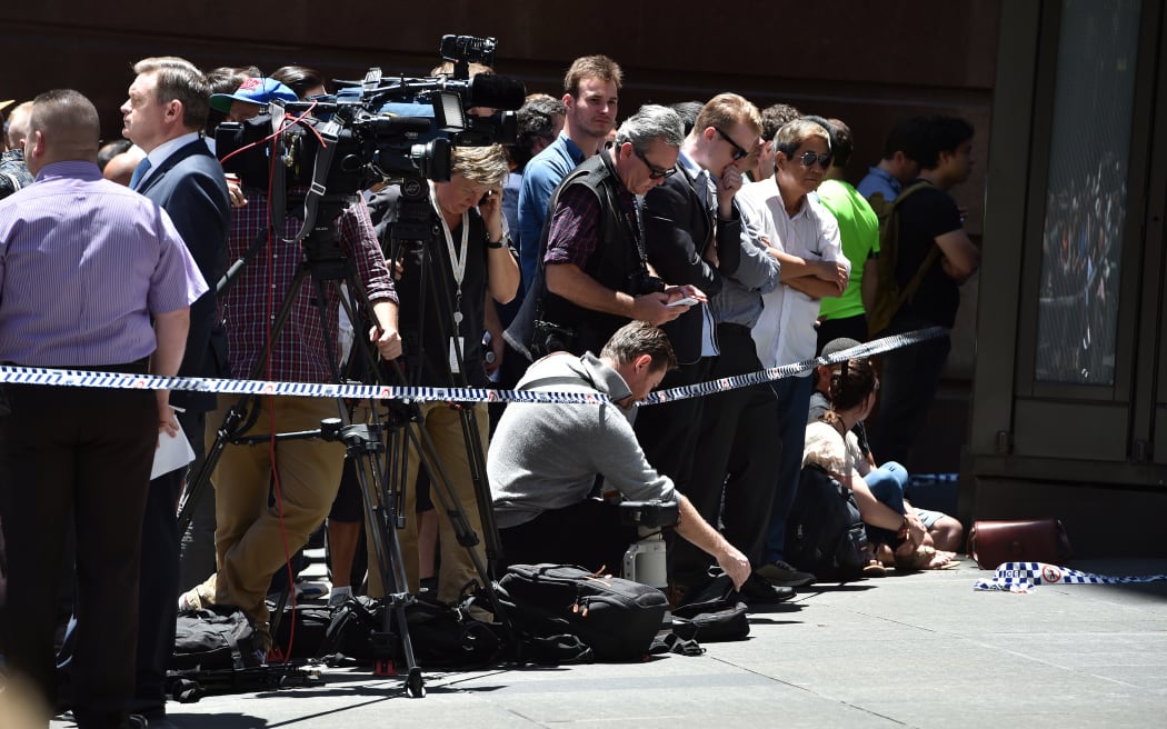 Members of the media monitor the situation near a cafe in the central business district of Sydney