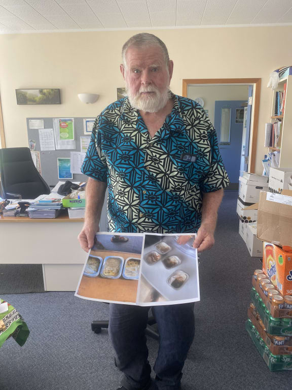 Massey Primary  principal Bruce Barnes holding photos of some of the lunches received under the new school lunch programme. 