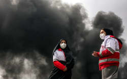 Women members of Iran’s Red Crescent society stand near smoke plumes from an ongoing fire following an overnight airstrike on the Shahran oil refinery in northwestern Tehran on March 8, 2026. The United States and Israel launched strikes against Iran on February 28, sparking swift retaliation by the Islamic republic which responded with missile attacks across the region. The war has dragged in global powers, upended the world’s energy and transport sectors, and brought chaos to even usually peaceful areas of the volatile region. (Photo by AFP)