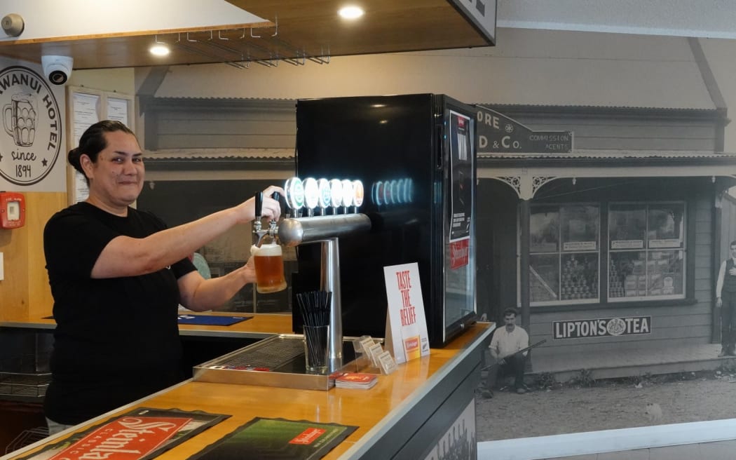General manager Kylie Wright pulls a pint at the refurbished Awanui Hotel, which is also decorated with historic photos.
