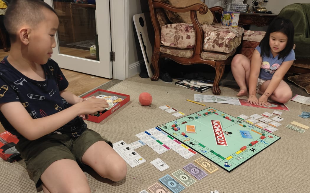 Raymond Hsu sits down in his home lounge, playing Monopoly with his sister.
