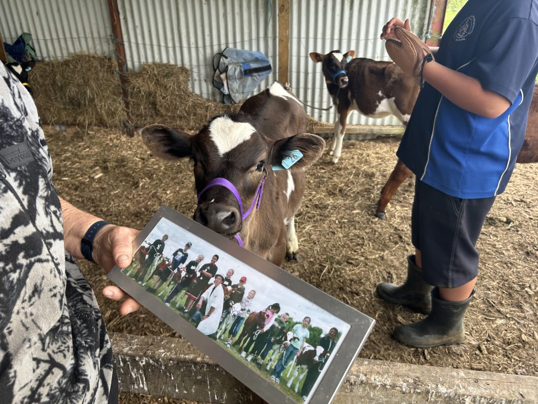 Photo depicts an old photograph sitting in a silver frame, the photo depicts Janet with a group of children and their calves.