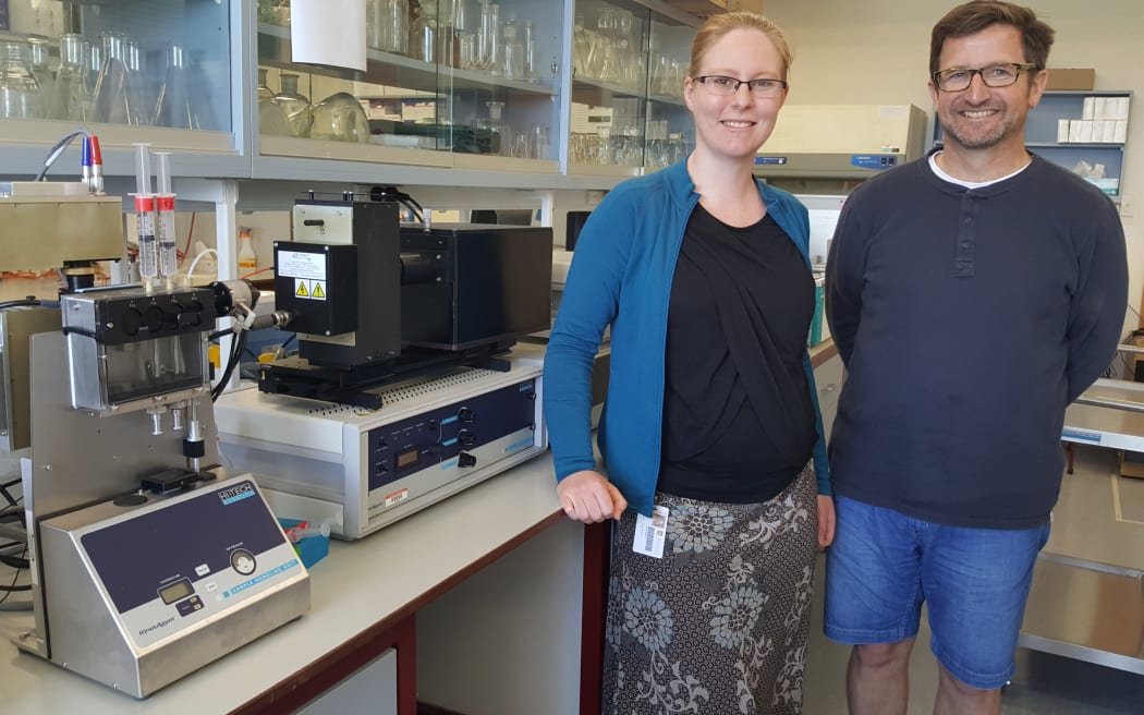 Erica Prentice and Vic Arcus in the lab, standing next to the machine they use to test enzyme reactions at different temperatures.