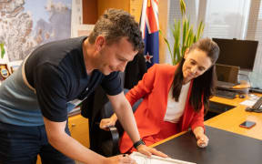 David Seymour and Jacinda Ardern with the signed transcript of her calling him an "arrogant prick" in Parliament. They plan to auction it off to charity.