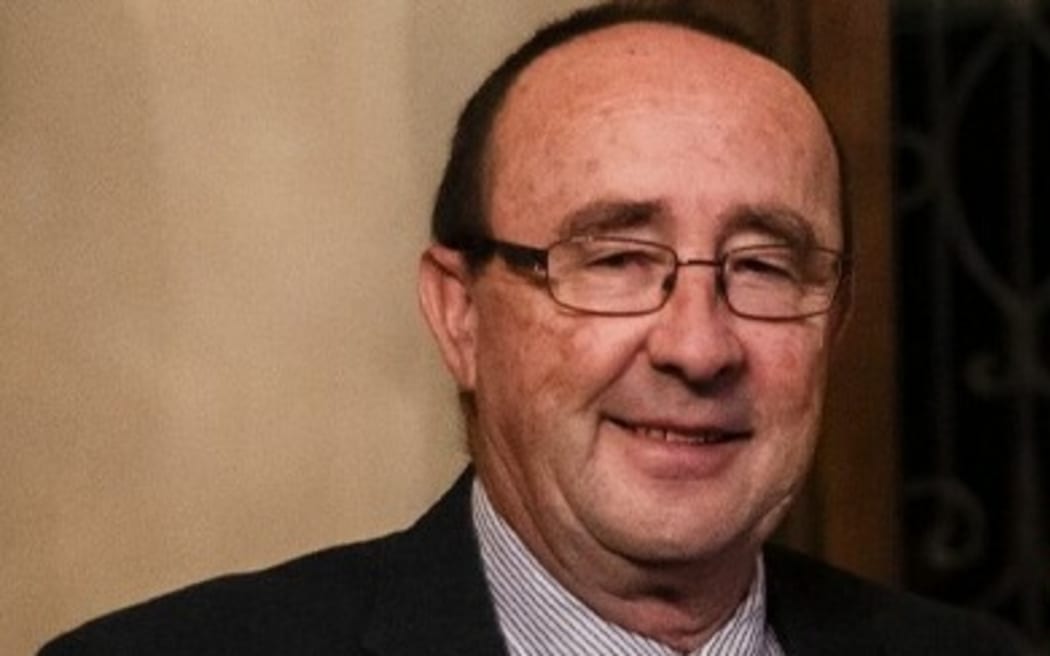A man in a suit and tie with glasses smiles at the camera.