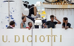 Migrants gather on the deck of the Italian Coast Guard vessel "Diciotti" in the Sicilian port of Catania, on August 23, 2018, as they wait to disembark following a rescue operation at sea.