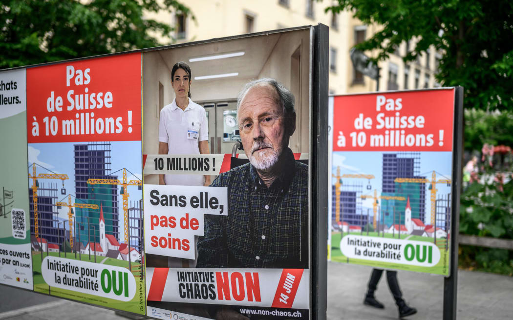 This photograph shows campaign posters for and against a nationwide vote on an anti-immigration initiative, reading (L and R) “No to a Switzerland of 10 million!” and (C) “Without her, there would be no care,” in Geneva on June 4, 2026. The Swiss will vote on June 14, 2026, on an initiative to cap the population at 10 million — an anti-immigration proposal that is fracturing public opinion in the wealthy Alpine nation. “No to a Switzerland of 10 million inhabitants,” is the name of the project launched by the country’s biggest party, the hard-right Swiss People’s Party (SVP), renowned for its opposition to immigration and closer ties with the European Union. (Photo by Fabrice COFFRINI / AFP)