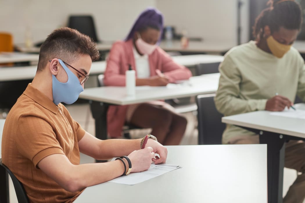 Side view portrait of young man wearing mask while taking test or exam in school with diverse group of people, copy space