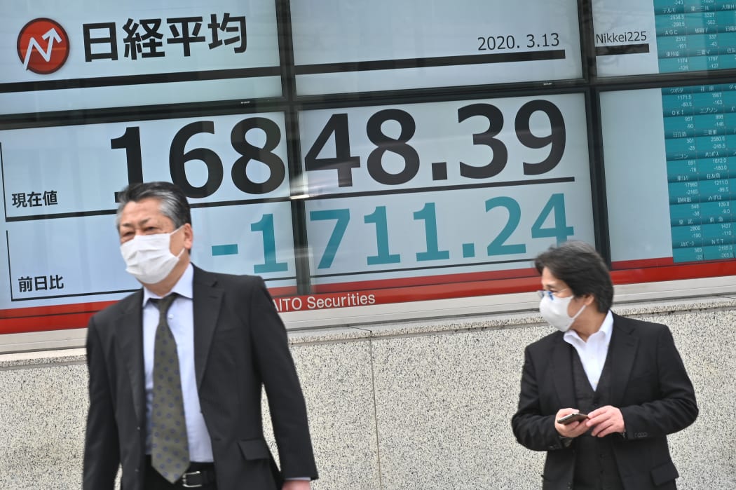Pedestrians walk past an electronic board showing the numbers for the Nikkei 225 index on the Tokyo Stock Exchange in Tokyo.