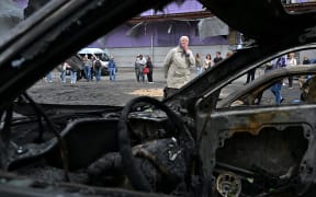 An elderly woman reacts as she looks at burned cars parked outside a mall following a night-time drone attack on Kyiv, on May 4, 2025 amid the Russian invasion of Ukraine. (Photo by Sergei SUPINSKY / AFP)