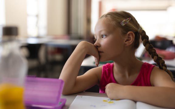 Child inside classroom, thinking, day dreaming.