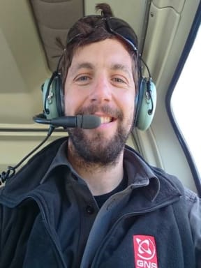 A man wearing a headset and headphones and a GNS fleece smiles at the camera.