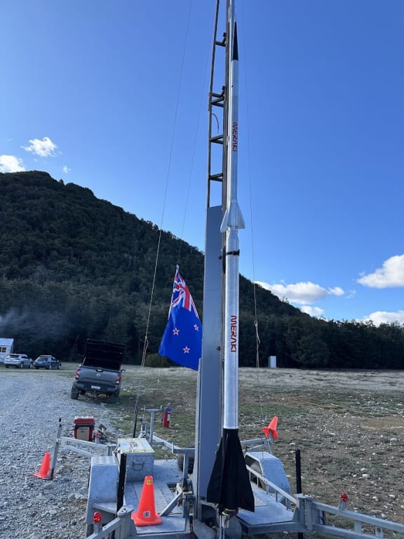 A rocket, in an open field, which is positioned ready for launch on a portable launch pad.