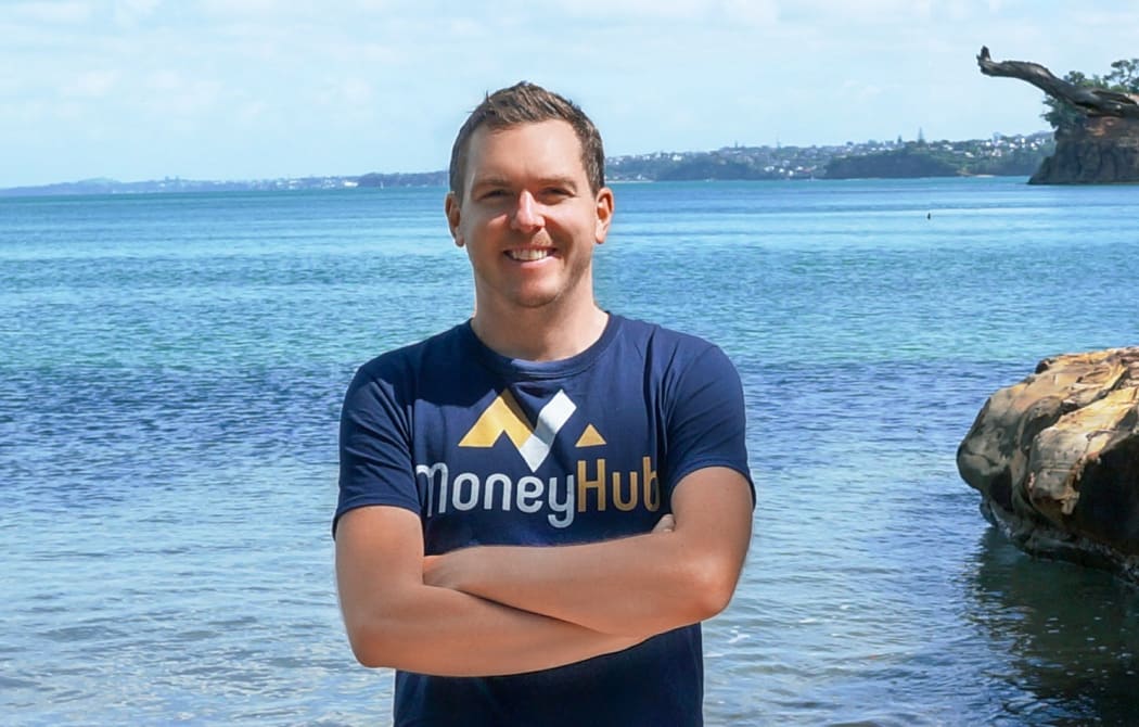 Photo of a man smiling at the camera, wearing a T-shirt with "MoneyHub" printed on it.