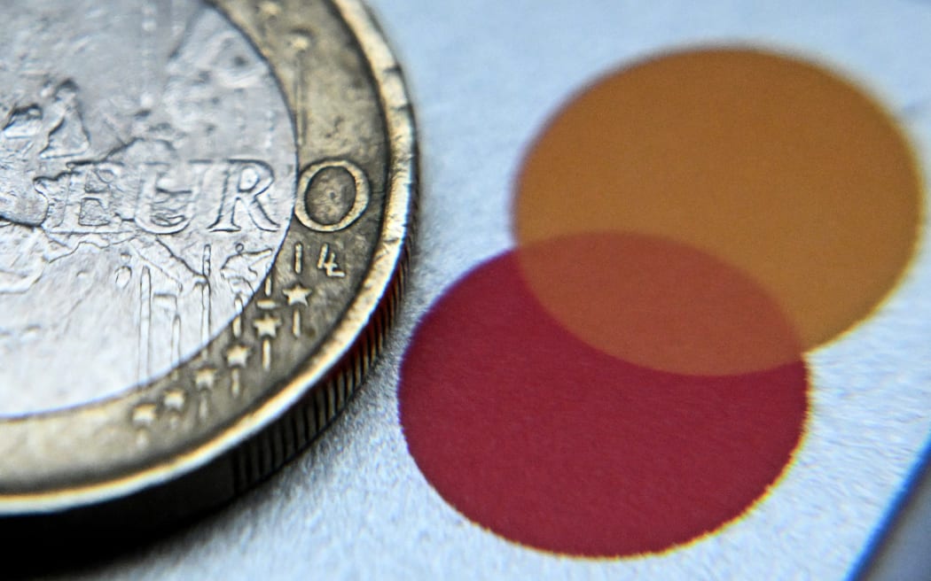 这张插图照片于 2023 年 12 月 22 日在德国西部美因河畔法兰克福拍摄，展示了万事达卡塑料银行卡上的欧洲欧元货币一欧元硬币。 （基里尔·库德里亚夫采夫/法新社摄）